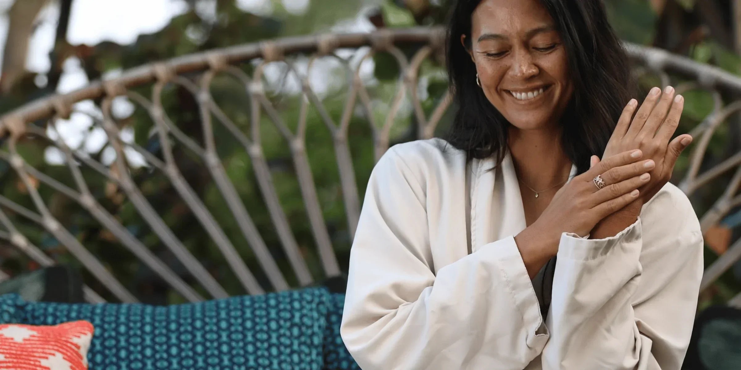 Woman sitting on couch rubbing lotion onto her hand while smiling