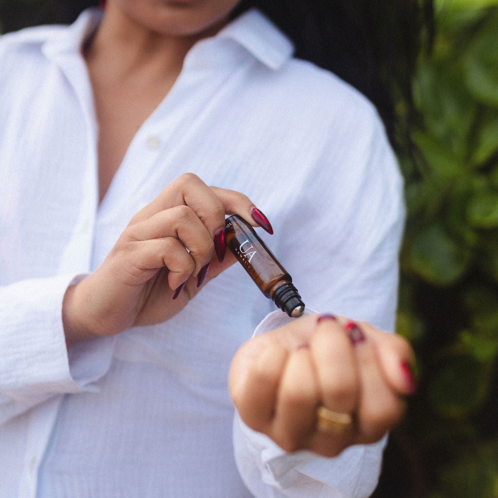 woman in white button down rolling perfume oil on wrist - travel size fragrance